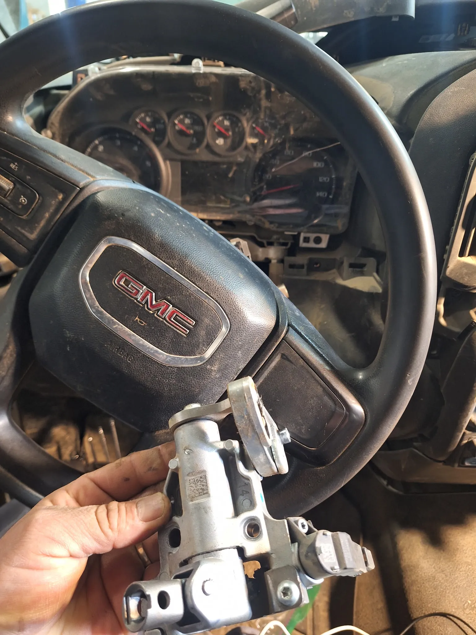 A disassembled ignition mechanism in front of a GMC steering wheel.