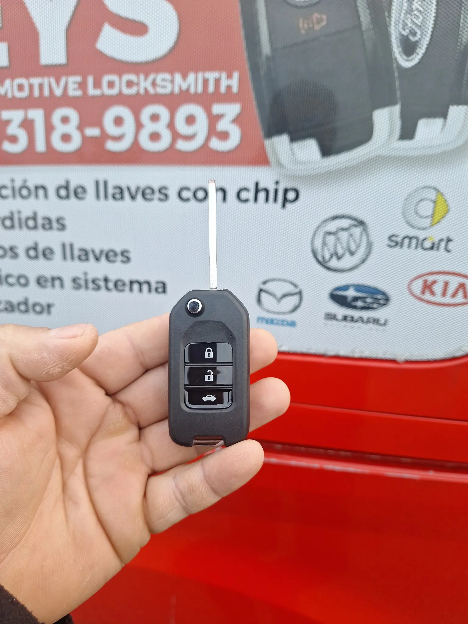 A car key in front of the Kano Automotive Locksmith vehicle.