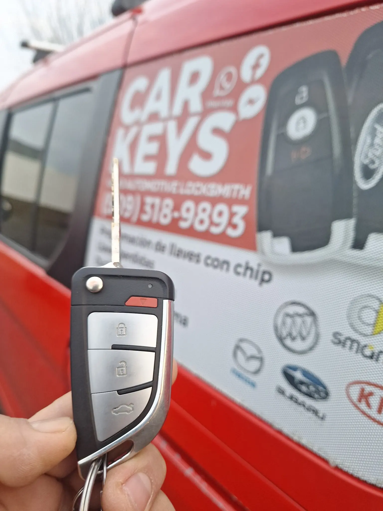 A car key in front of the Kano Automotive Locksmith vehicle.